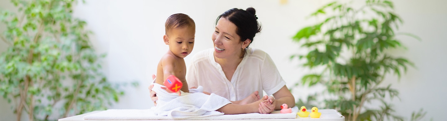 Madre sonriente jugando con su bebé envuelto en una toalla blanca después del baño.