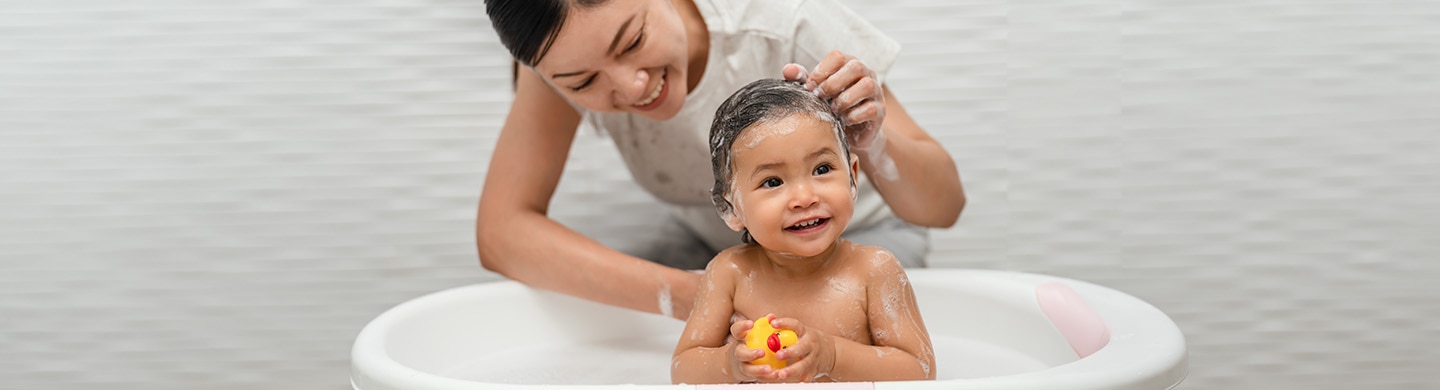 Madre lavándole el cabello a su bebé sonriente en una tina infantil con un patito de hule.