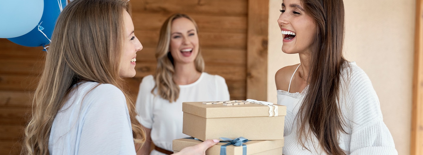 Mujer sonriente recibe regalos de sus amigas en un evento con globos azules.